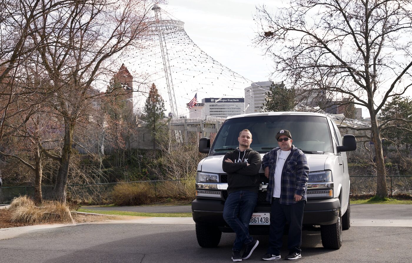 Ben and Greg from Precision Lock & Key standing in front of their service van in downtown Spokane with the Pavilion in the background