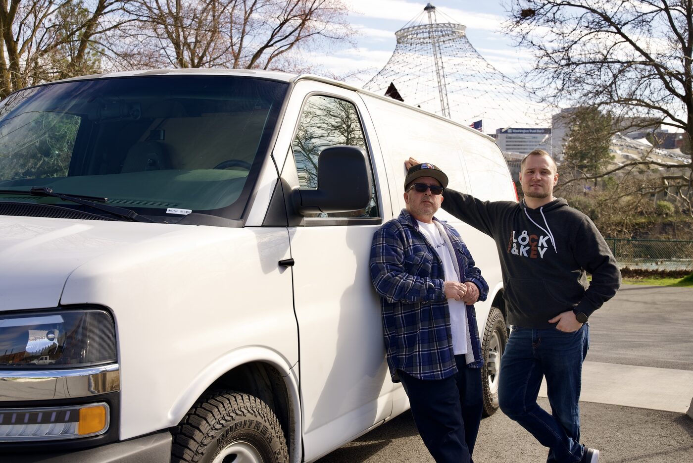 Greg and Ben of Precision Lock & Key leaning against their work van with the Spokane Pavilion behind them